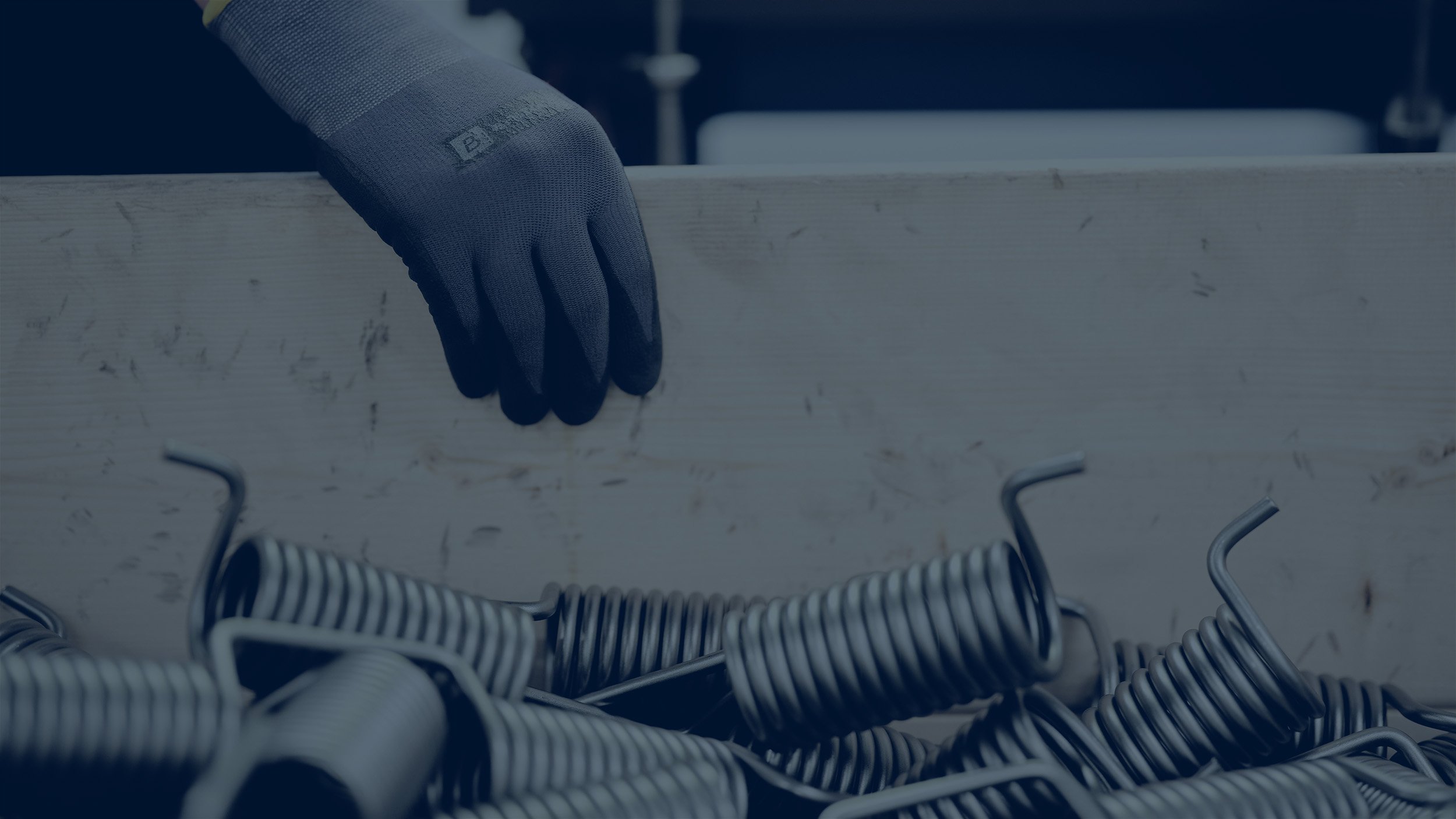 A worker wearing gloves handling a crate filled with Lesjöfors metal springs in an industrial environment.