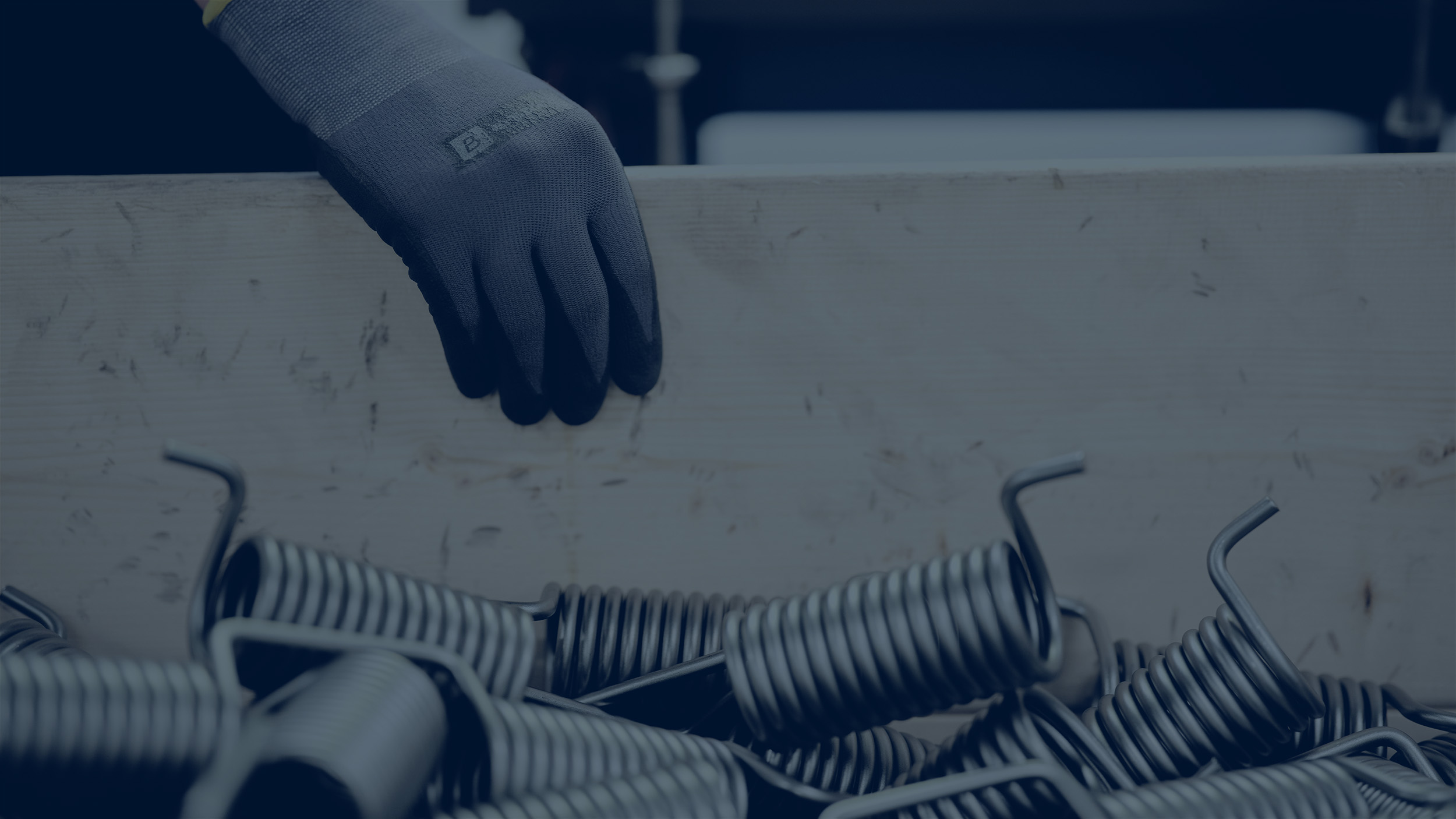 A worker wearing gloves handling a crate filled with Lesjöfors metal springs in an industrial environment.