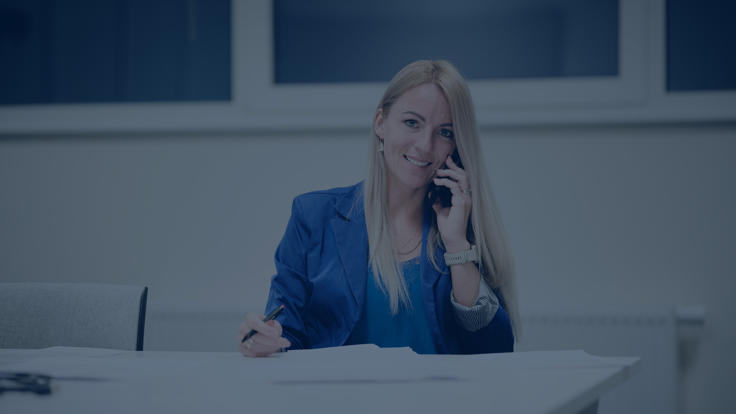 Rappresentante del servizio clienti di Lesjöfors che indossa una giacca blu, seduto a una scrivania, parlando al telefono e prendendo appunti, fornendo supporto professionale.