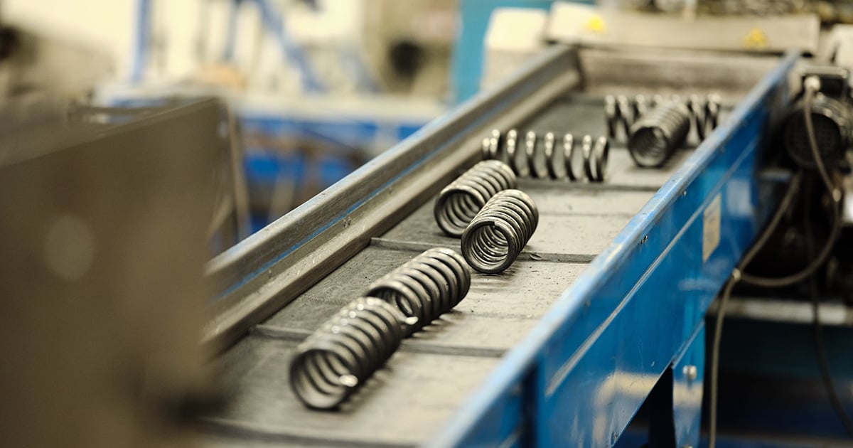 Close-upbeeld van een transportband die opgerolde metalen veren verplaatst in een industriële omgeving.